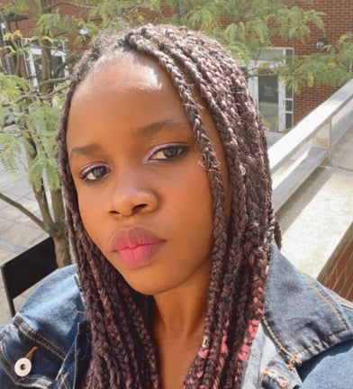 Adachioma Ezeano looks directly at the camera, her hair in braids, she wears a denim jacket.