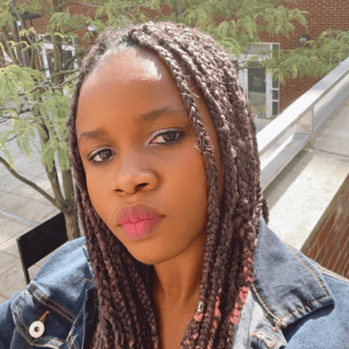 Adachioma Ezeano looks directly at the camera, her hair in braids, she wears a denim jacket.
