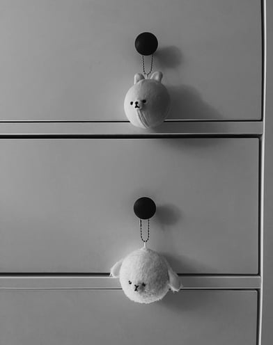 two stuffed toy keychains from the brand Mofmo Friends are hanging on the knobs of a dresser