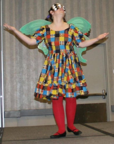 woman wearing patchwork dress, red tights, fairy wings, and mask while striking heroic pose