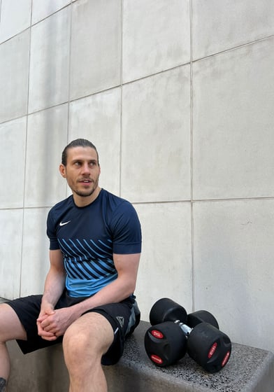 A personal trainer sat with dumbbells at his side