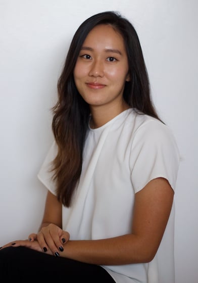 Ashley Sojin Kim sits with her hands crossed in her lap, wearing a white shirt and black pants.