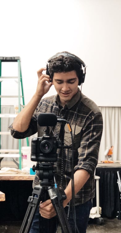 a man in a plaid shirt and headphones on a tripod recording video