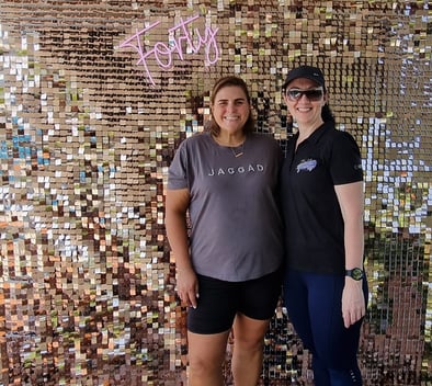 Carly and Linelle, standing in front of a rose gold shimmer wall with a ‘Forty’ neon sign, for her birthday in Brisbane.