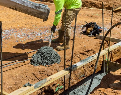 a man in a yellow jacket is pouring concrete into a concrete slab