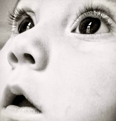 Black and white close-up of a baby girl's face, looking upward with wide eyes, capturing a sense of wonder and innocence