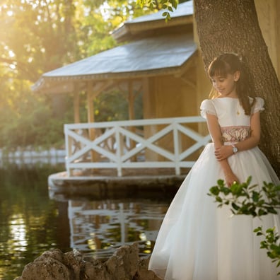 niña con vestido comunion posa en exterior del lago mirando al suelo y sonrriendo  