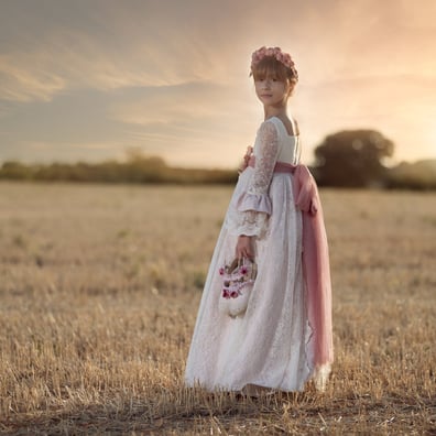 niña posa mirando atras con vestido de comunion y poniéndose el sol  