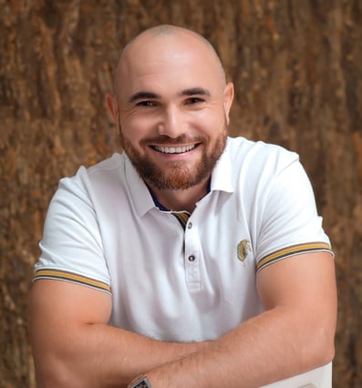 Un homme chauve de 40 ans souriant, en polo blanc assis sur une chaise