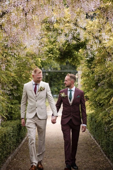 Two men holding hands whilst walking through a garden on their wedding day