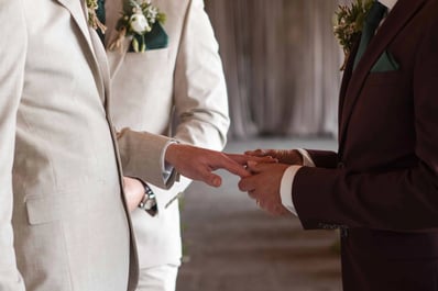 man slides ring onto his husbands hand on their wedding day