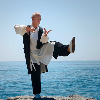 Esat Ataç performing a 36 Form Tai Ji Quan posture by the sea, in traditional Wudang attire.