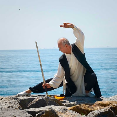Esat Ataç performing a Wudang sword (Jian) form on seaside rocks, in a low focused stance.