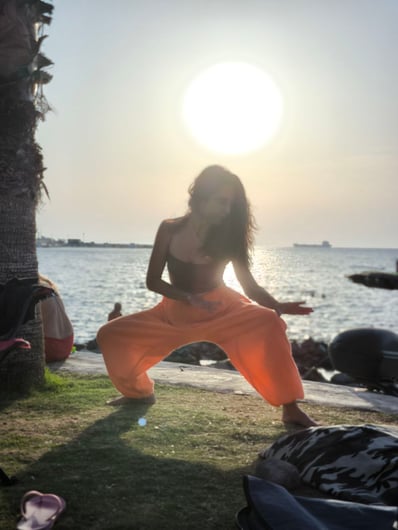 Gizem Kara practicing Tai Ji at sunset by the sea, in taming tiger stance, glowing in backlight.