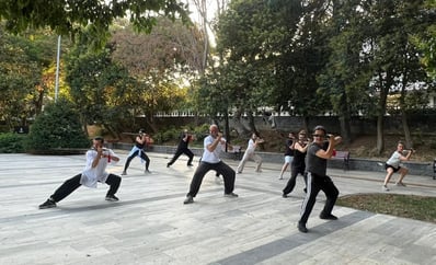 Mehmet Başkak leading a Wudang sword group training outdoors at İnönü Park under the trees.