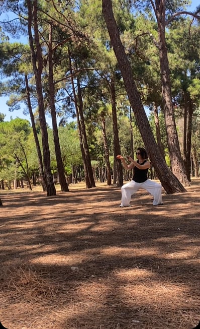 Mine Şilliler flows like wind through the pines, her stance steady, rooted in shifting light.