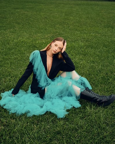 Full-body shot of model in a blue ruffle suit sitting on grass, styled for a fashion editorial.