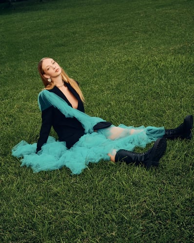 Full-body shot of model in a blue ruffle suit sitting on grass, styled for a fashion editorial.