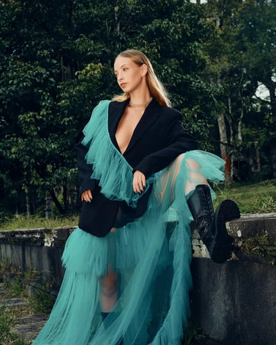 Full-body shot of model in a blue ruffle suit standing with one leg raised to highlight black boots.