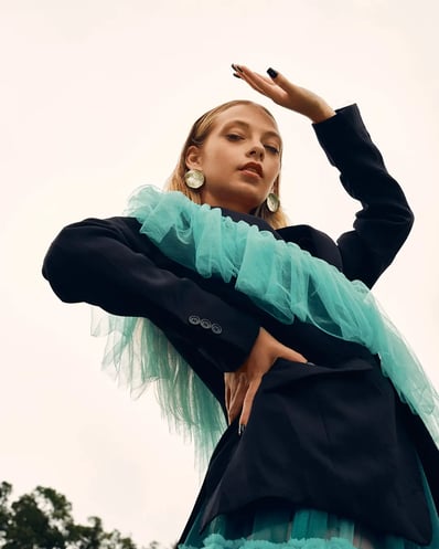 Portrait of model in a blue ruffle suit, shot from a low angle to showcase the sky, styled for a fashion editorial.