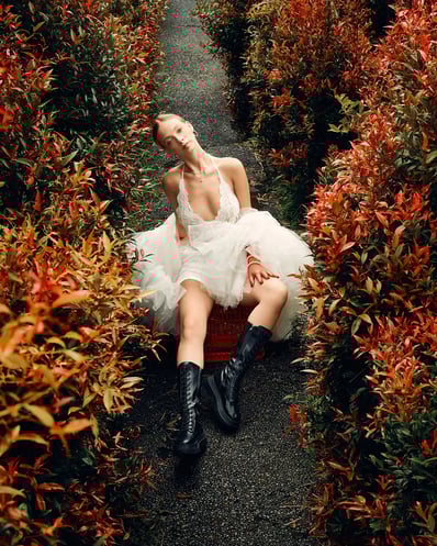 Full-body editorial shot of model in a white lace top sitting among red flowers in Bali.
