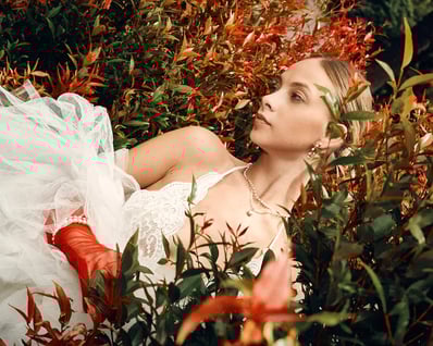 Portrait of model in a white lace top with red flowers in the foreground, captured for a fashion editorial.