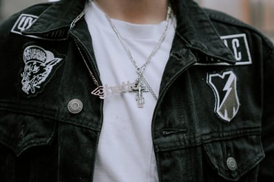 un homme portant une veste en jeans noire avec des patchs dessus, un t-shirt blanc et des colliers argentés