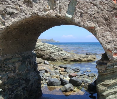 Arcade rocheuse en forme de rond par lequel on aperçoit des rochers et la mer toute bleue