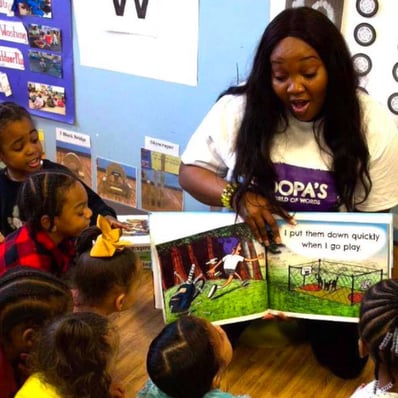 Preschool students around a teacher reading OOPA's World.