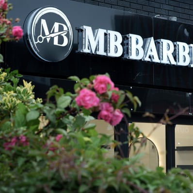 the front entrance of a black barber shop taken from behind a pink flower rose bush