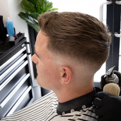 Barber cutting a customers hair while he is relaxed in a barber chair with a striped cape
