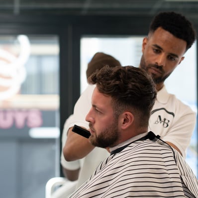 Side View of a customer having his hair cut by a barber while sat in a striped gown
