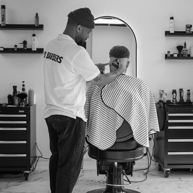 black and white image of barber with company T-shirt grooming a customer with clippers