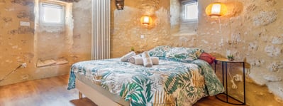 Chambre du moulin vue en grand angle, deux fenêtres, serviettes et éclairage mural mis en valeur