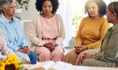 Mulheres participando de encontro projeto Maria's reunidas em oração com Bíblia aberta à frente.