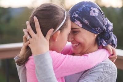 a smiling woman in a purple head wrap and a girl in a pink shirt embracing