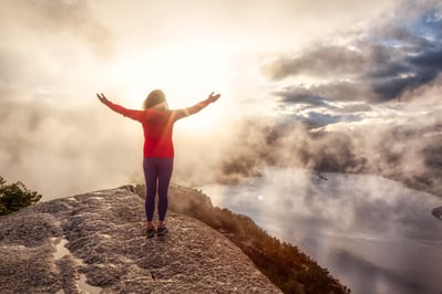 a person is standing on cliff with her arms outstretched out to the sky