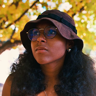 Young college black woman birdwatching underneath golden yellow autumn trees.