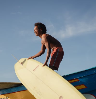 Surfer with a yellow board on boat at a surf school in Kuta Lombok. He is enjoying a surf lesson.