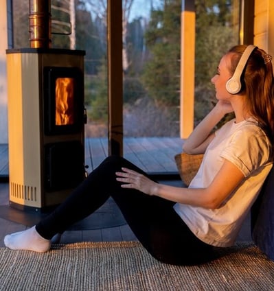 Estufa de pellets con fuego perfecta con mujer escuchando musica con cascos en el suelo de una casa
