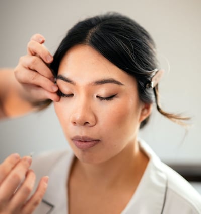 Makeup artist adjusting a false lash during application on the bride.