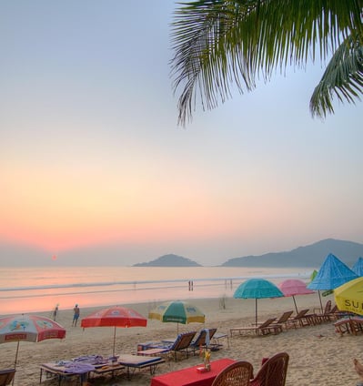 Beach with sunset and people walking along the beach with umbrellas to sit