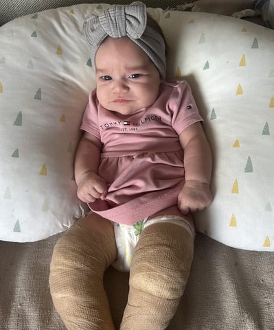 a baby girl in a pink outfit is sitting on a pillow
