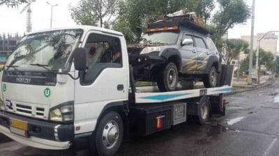 Caminhão branco, tipo plataforma, carregando um veículo de trilha ou rally, o asfalto está molhado.