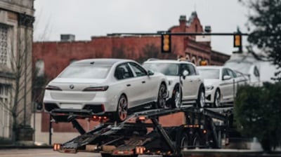 Cegonha ou carreta de transporte de veículos, trafegando por um bairro estilo antigo.