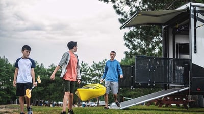 a group of people walking around a trailer carrying a canoe