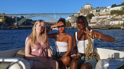 Three girls posing for a photo on the Endure speedboat with Dom Luís I Bridge in the background