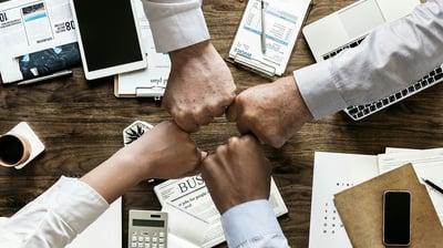 two people shaking hands over a desk with a laptop