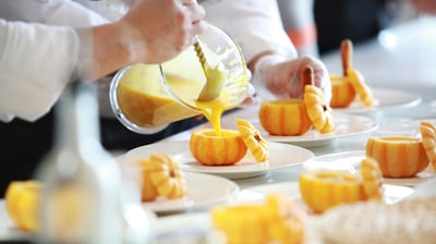 a person pouring a sauce on a plate with small pumpkins