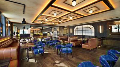 Modern restaurant interior with blue chairs and geometric lighting.